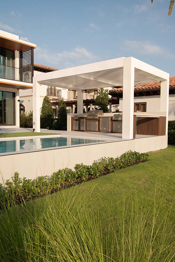 White louvered pergola over the pool with high-end outdoor kitchen - Azenco Outdoor, R-Blade model.