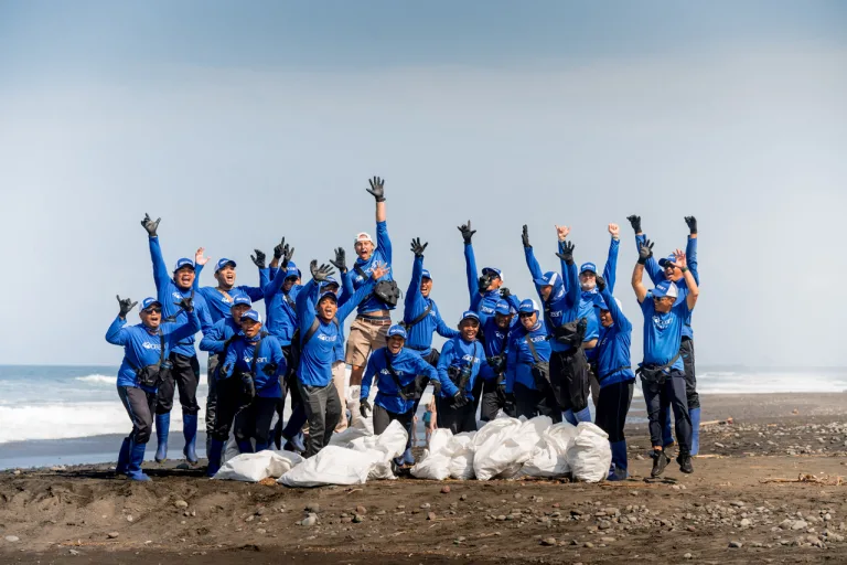 The 4ocean cleanup team cheering on a beach, surrounded by large white bags of recovered ocean-bound debris and plastic pollution.