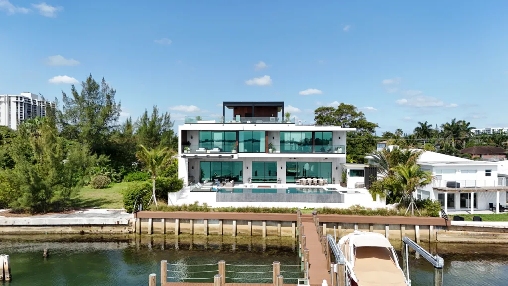 Modern luxury waterfront home featuring a black R-Blade™ pergola on the rooftop terrace and boat dock below.