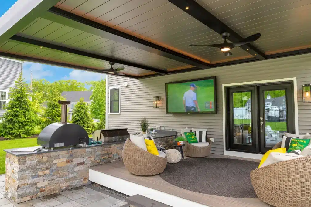 Outdoor kitchen with stone masonry, built-in pizza oven, grill, sink, and a black Azenco pergola overhead.