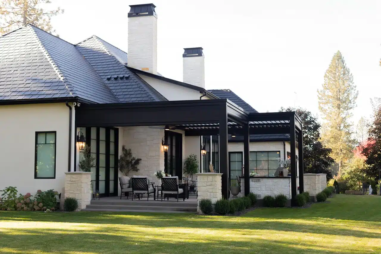 Luxury home exterior with Azenco R-Blade™ louvered pergola featuring a black aluminum frame and white stone columns over a paved patio.