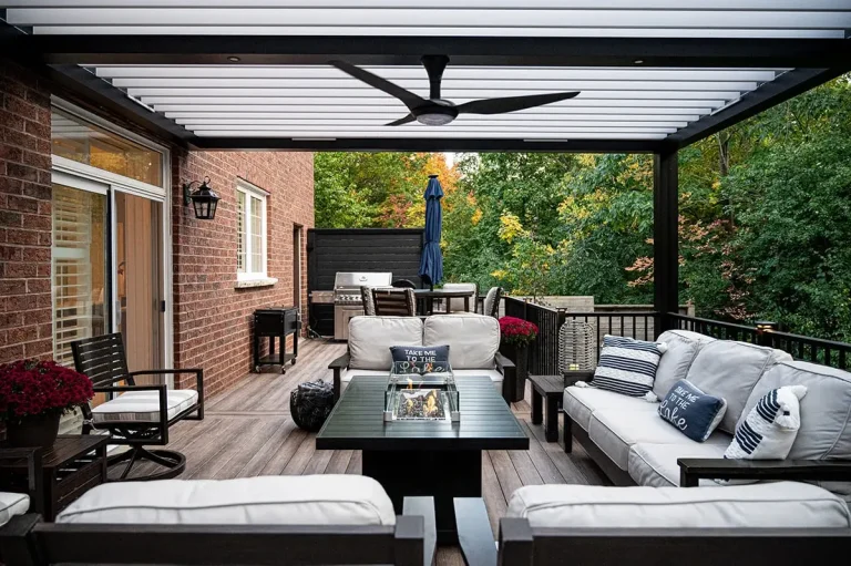 Black louvered pergola with white louvers and a ceiling fan over a deck lounge with a fire table