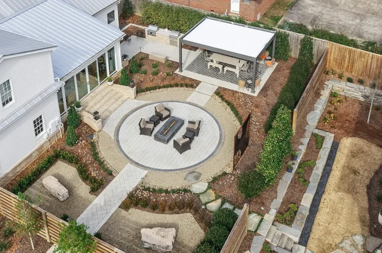 Aerial view of a gray and white R-SHADE™ patio cover in a landscaped backyard with a round fire pit