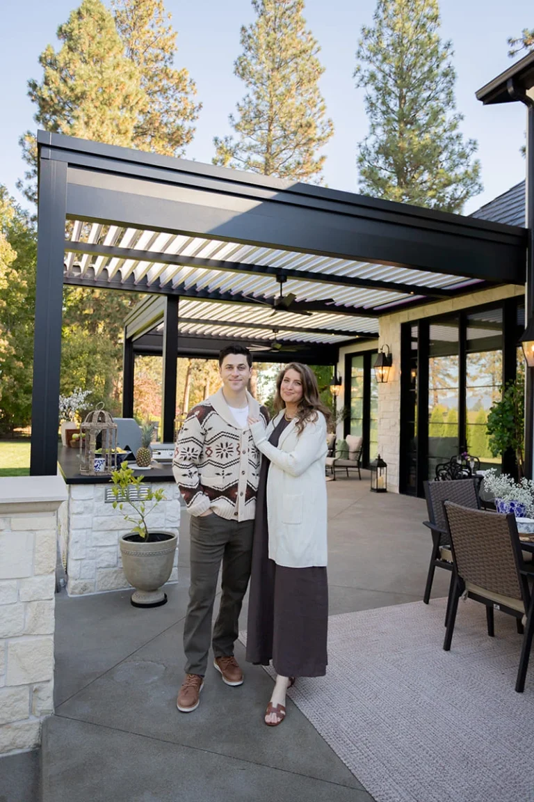 Homeowners standing under their black louvered pergola