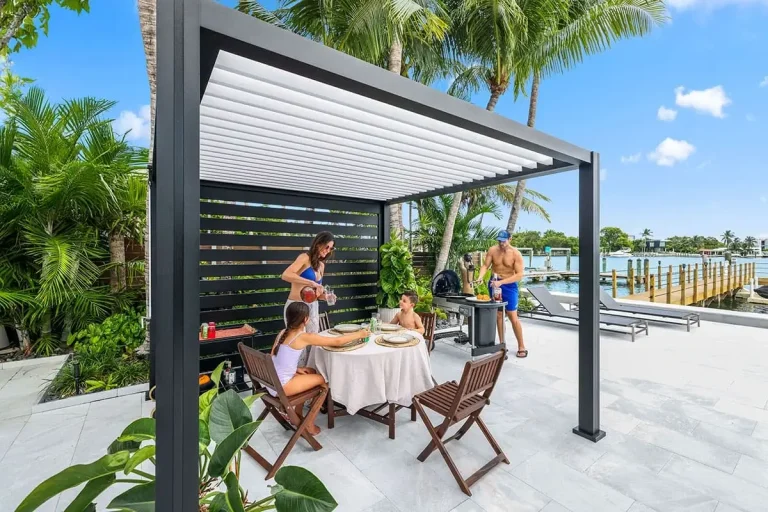 Black K-BANA™ pergola with white louvers and privacy wall over a poolside dining table