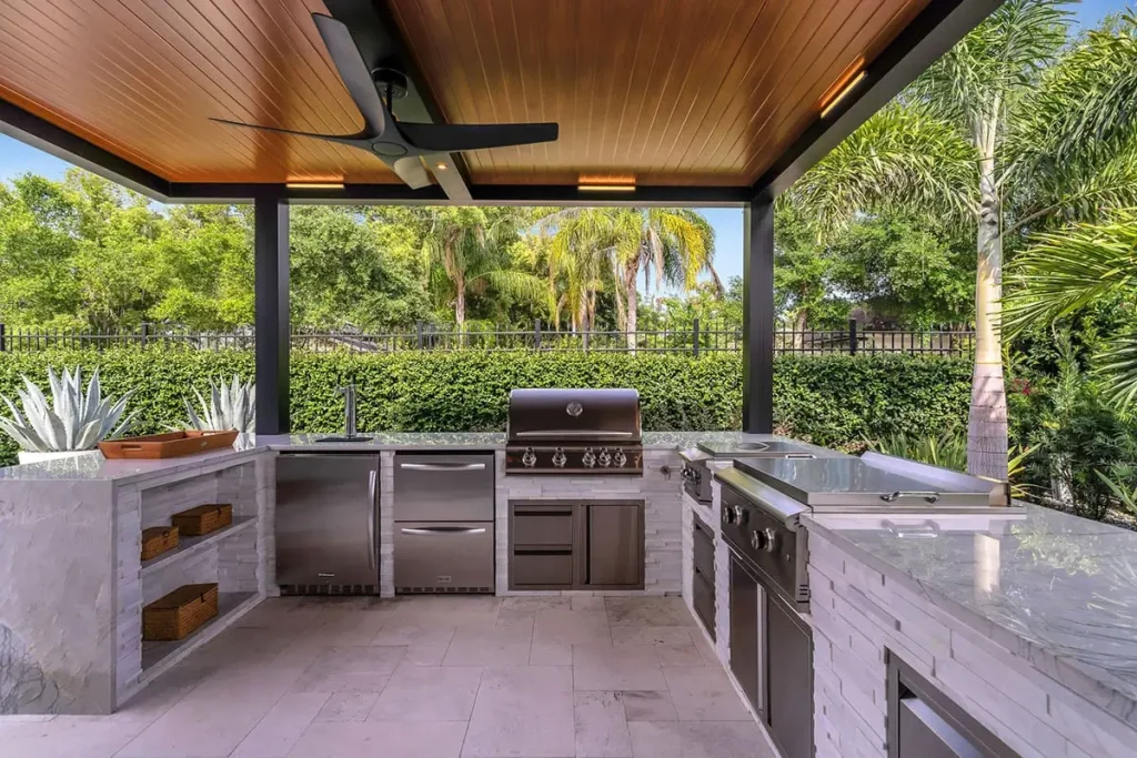 Black R-SHADE™ insulated patio cover with wood-grain ceiling, fans and LED lights over an outdoor kitchen