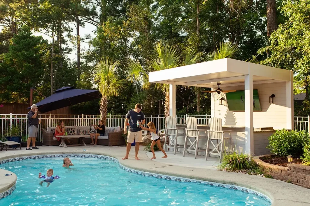 White R-SHADE™ patio cover with an outdoor bar and TV beside a family pool